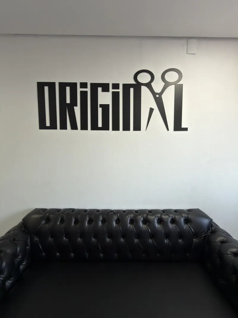 Parede com a logo da Original Barbershop e sofá de couro na recepção